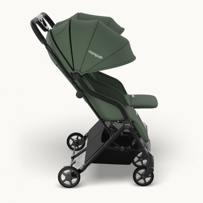 A compact double stroller in sage green fabric with a black frame and wheels, shown from a side profile on a light gray background. The brand name 'monpush' is visible on the canopy.