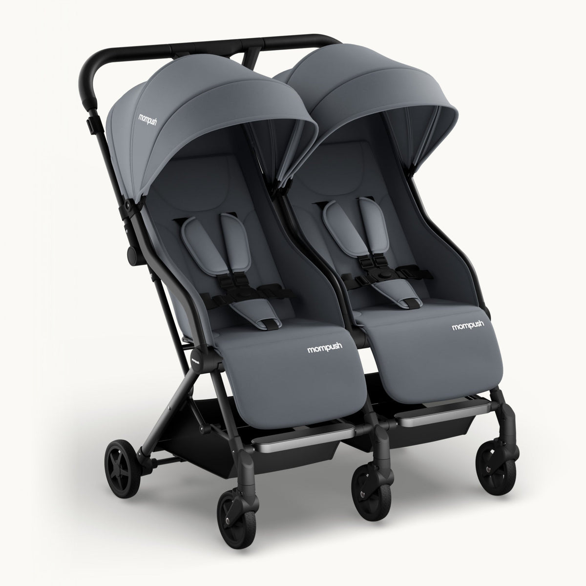 A compact double stroller in dark gray and black, shown from a three-quarter front angle on a light off-white background. The stroller features two separate infant seats with built-in canopies, padded harness straps, and the 'monopush' brand name printed in white on the front of each seat.