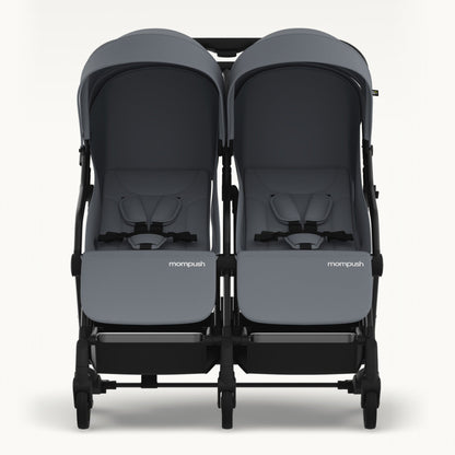 A front-facing view of a double stroller with dark gray fabric seats and canopies, a black frame, and the 'mompush' logo on the front of each seat, set against a plain off-white background.