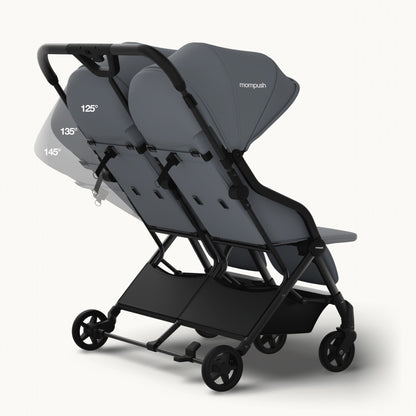 A compact double stroller in dark gray and black, shown from a three-quarter angle on a light gray background. The stroller features two seats with adjustable reclining backs, a large canopy, and a storage basket underneath.