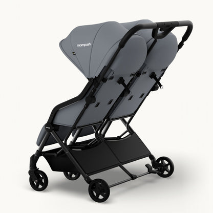A compact double stroller in gray and black, shown from a three-quarters angle on a clean, light off-white background. The brand name 'monpush' is visible on the canopy.