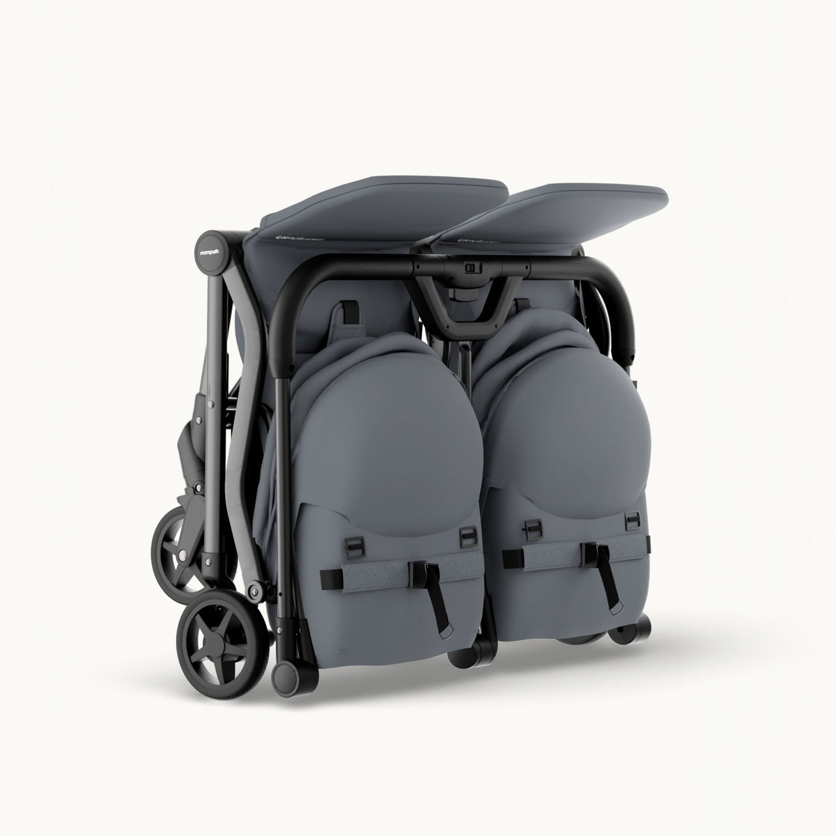A folded double stroller in dark gray fabric with a black frame and wheels, shown from a three-quarters angle on a light off-white background.