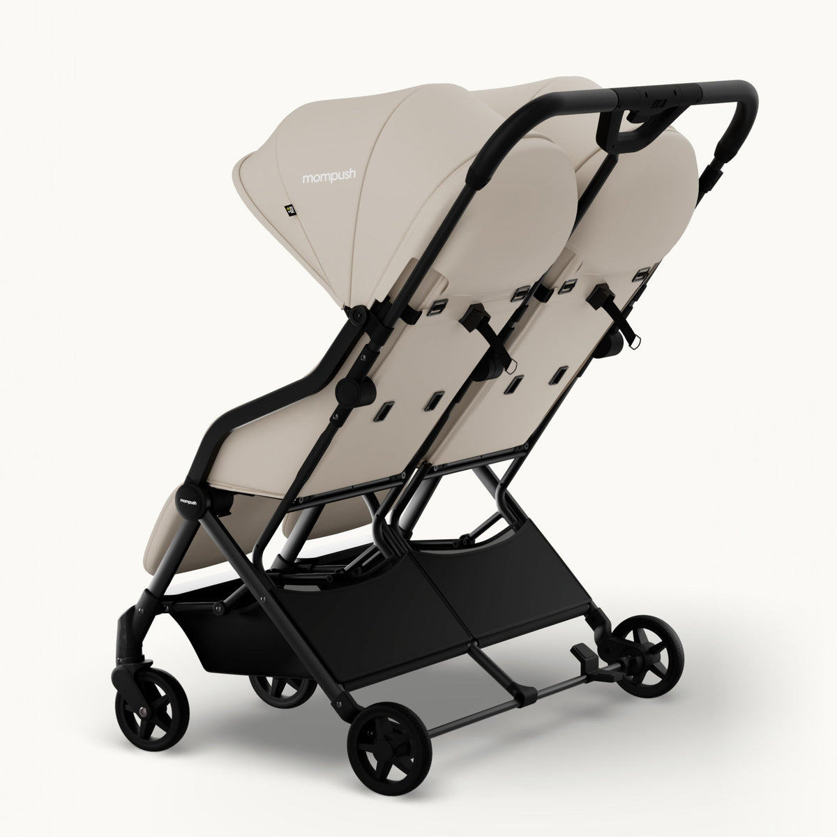 A compact double stroller in a light beige fabric with a black frame, shown from a three-quarters angle on a clean white background. The brand name 'monpush' is visible on the canopy.