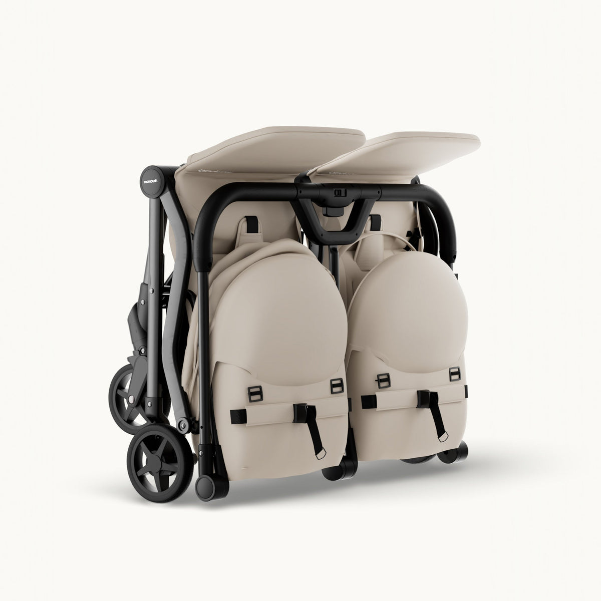 A compact, folded double stroller in a light beige fabric with a black frame and wheels, shown from a three-quarters angle on a clean, off-white background.