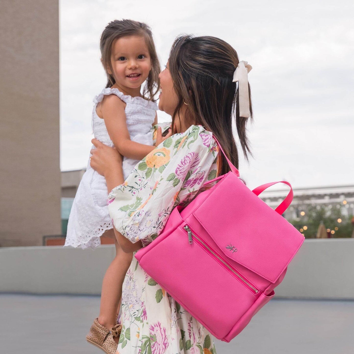 Woman holding a child and carrying Freshly Picked Hot Pink Mini Classic Diaper Bag II outdoors