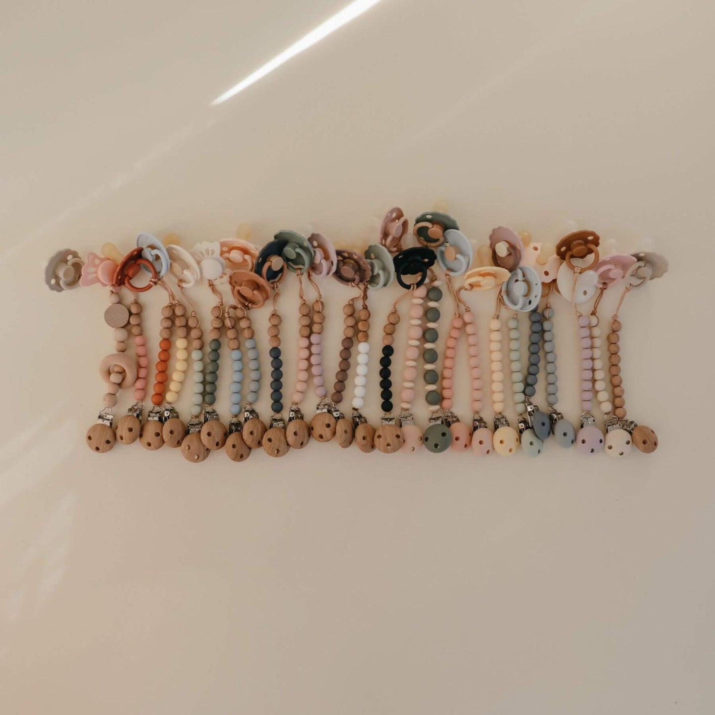 Row of colorful Mushie FRIGG Silicone Pacifiers with rings on a white surface