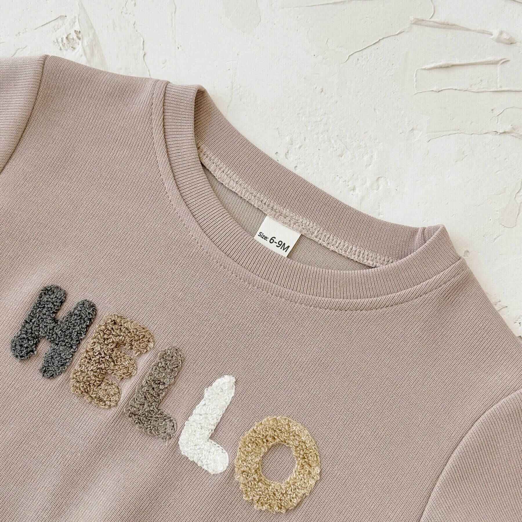 Beige sweatshirt with 'HELLO' in fabric letters on a textured beige background