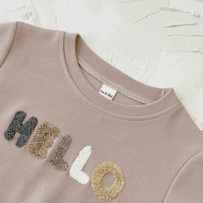 Beige sweatshirt with 'HELLO' in fabric letters on a textured beige background