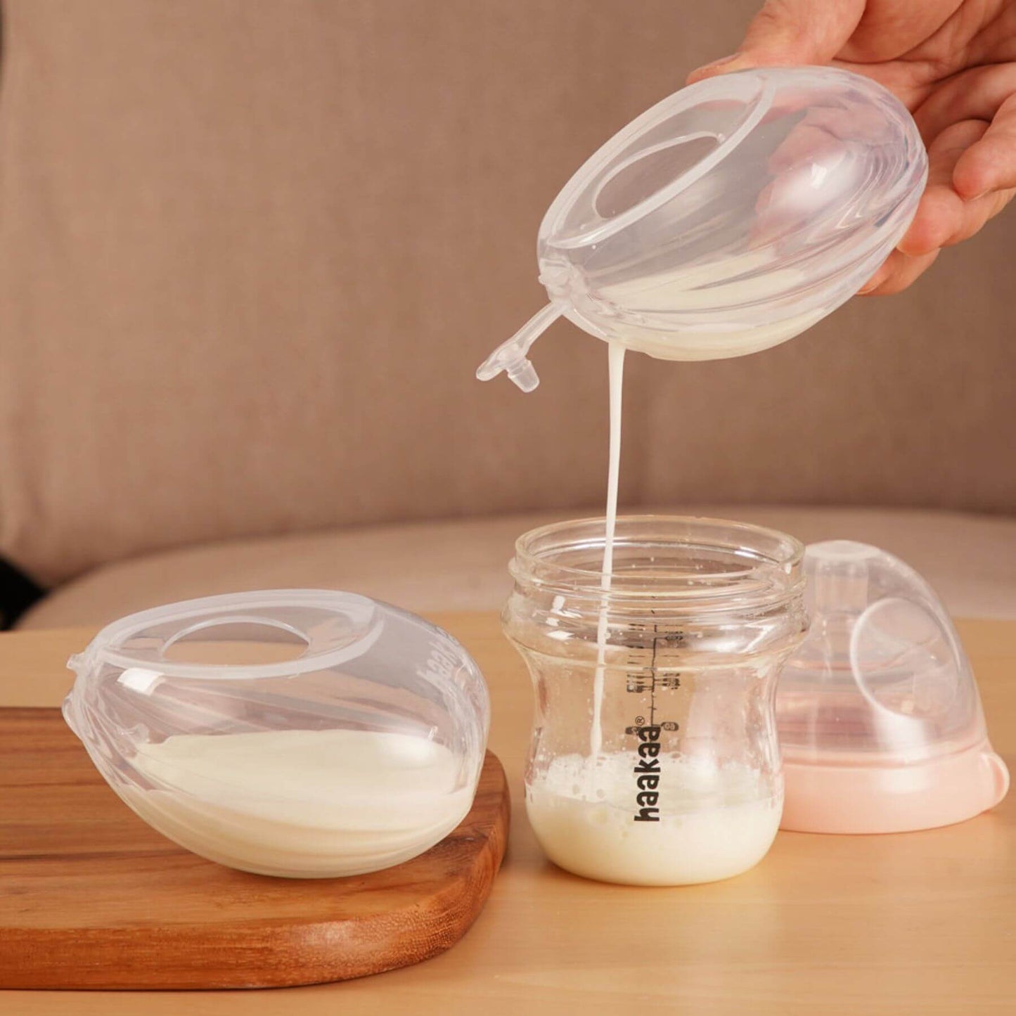 Person pouring milk from a silicone container into a glass jar on a wooden surface.