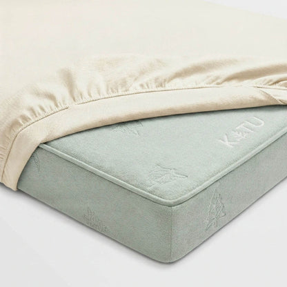 A close-up of a mattress fitted with a light beige sheet, showing the mattress corner and the brand name KATU embossed on the side.