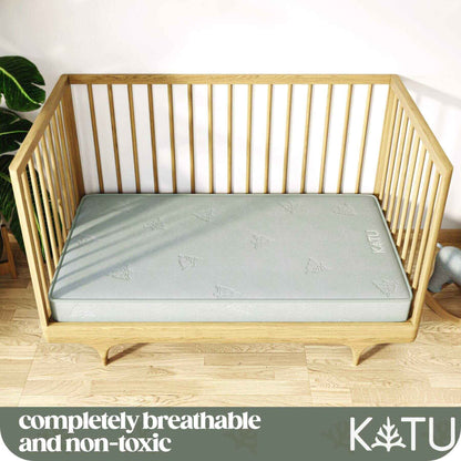 Wooden crib with KATU Organic 2-Stage Crib Mattress in a room with a plant and toy.