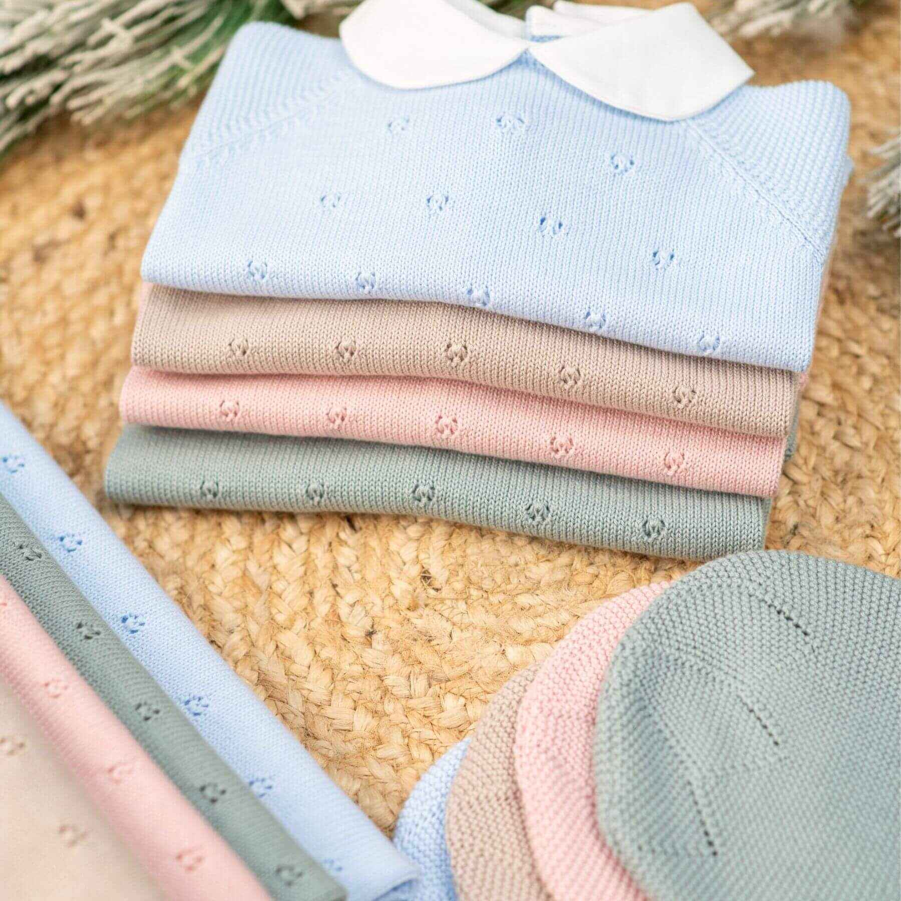 Stack of folded baby sweaters in pastel colors on a textured surface