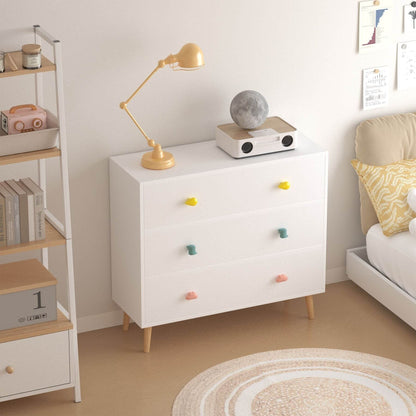 White dresser with colorful knobs in a room with a lamp and books.