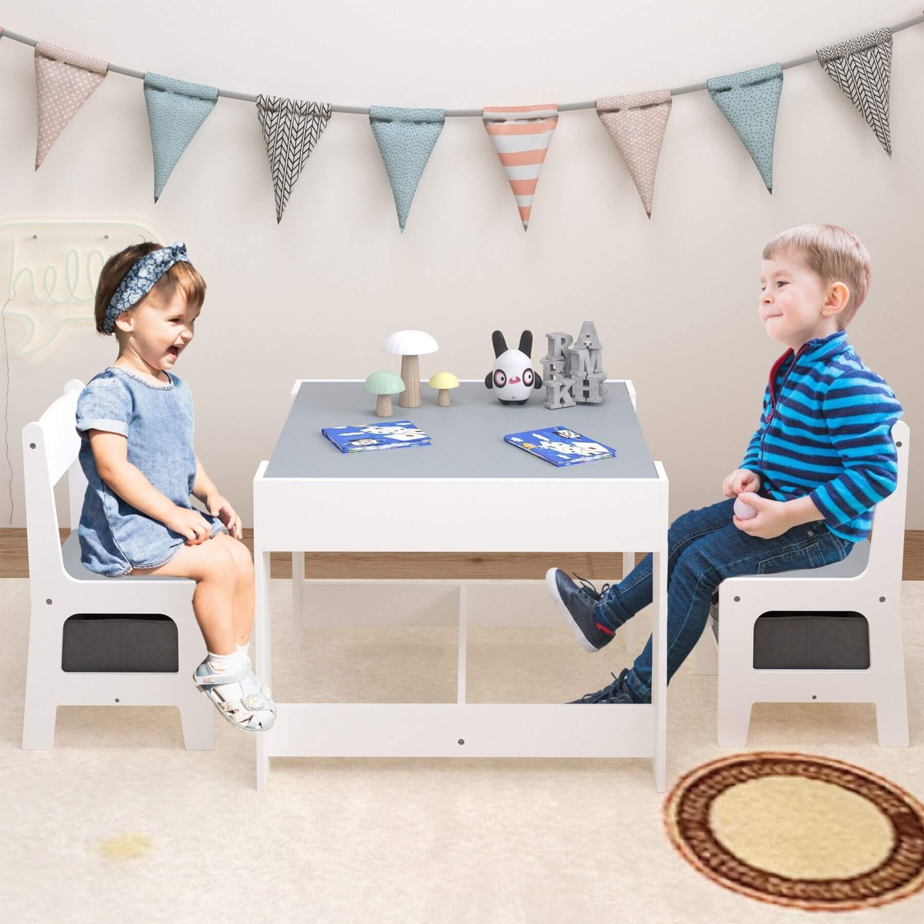 Two children sitting at a small table with toys in a playroom setting.