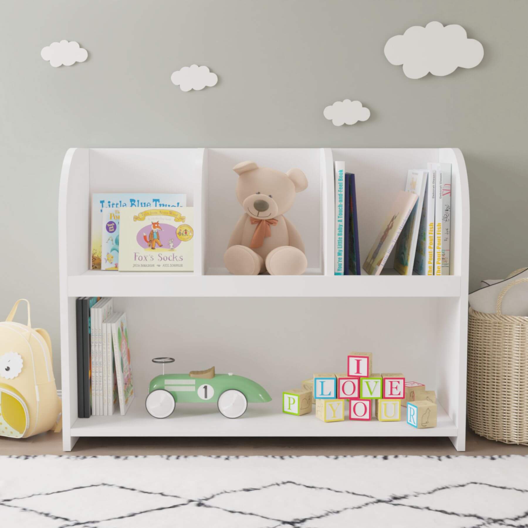 White children's bookshelf with books, a teddy bear, and toys against a gray wall with cloud decorations.