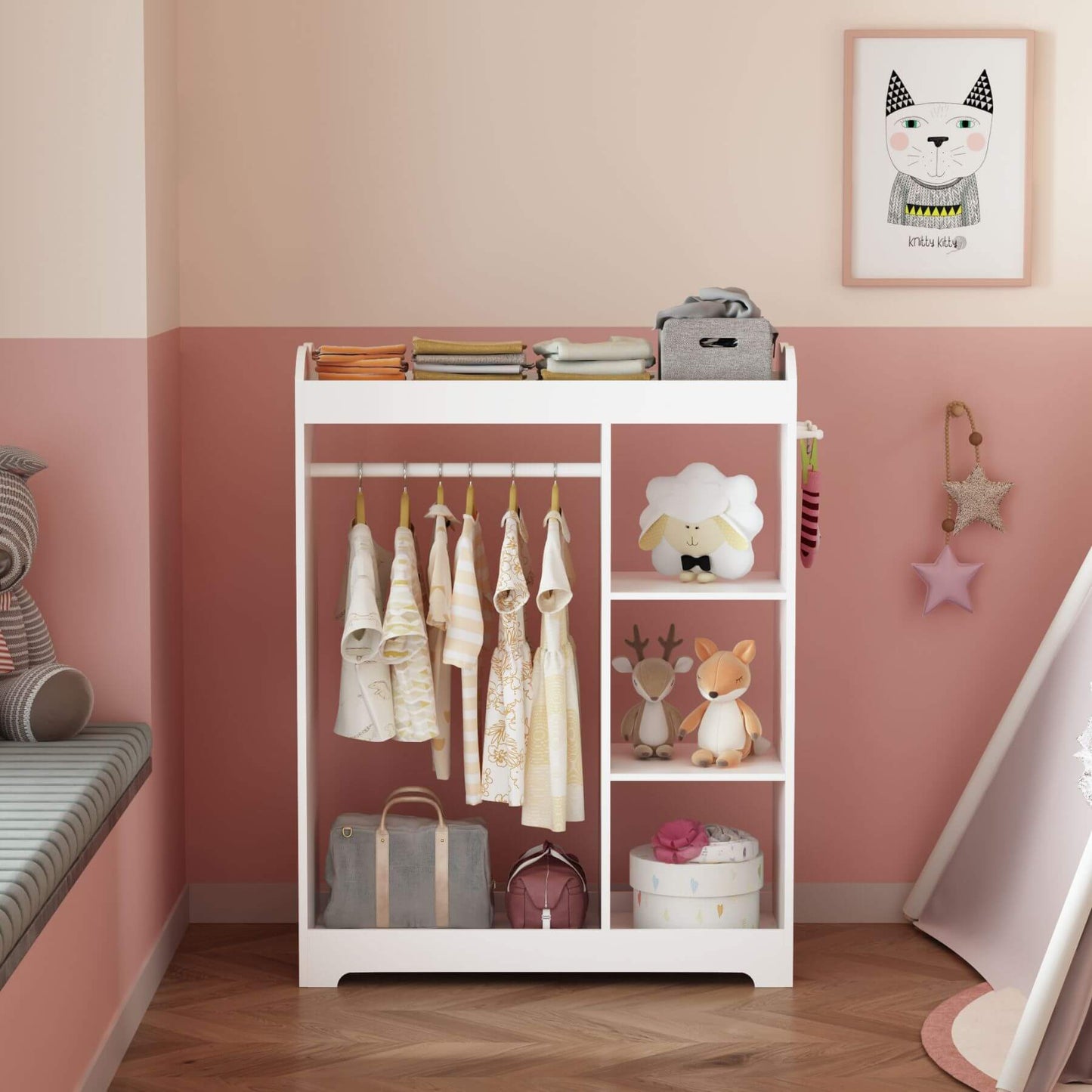 White children's clothing rack with clothes and toys against a pink wall.