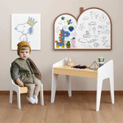 Child sitting at a small table with drawing boards on the wall in a room.