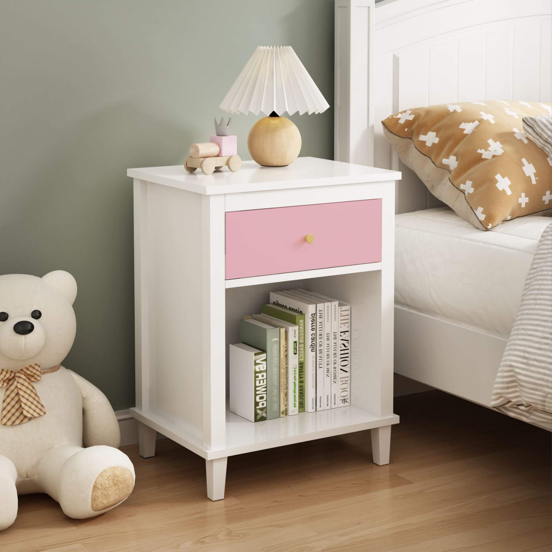 MOONRIVER Golden Handle Wooden Nightstand - Pink next to a bed with a teddy bear and books on a wooden floor.