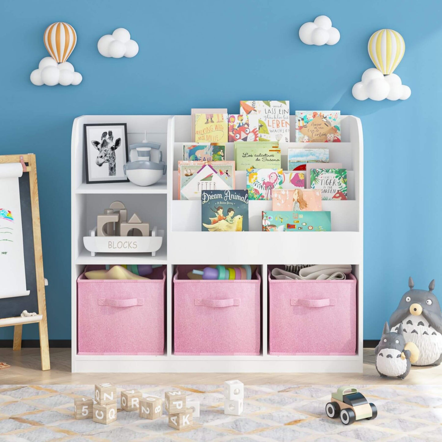Children's room with MOONRIVER Kids Bookcase with 3 Collapsible Fabric Drawers - White/Pink, and children's toys against a blue wall with cloud and balloon decorations.