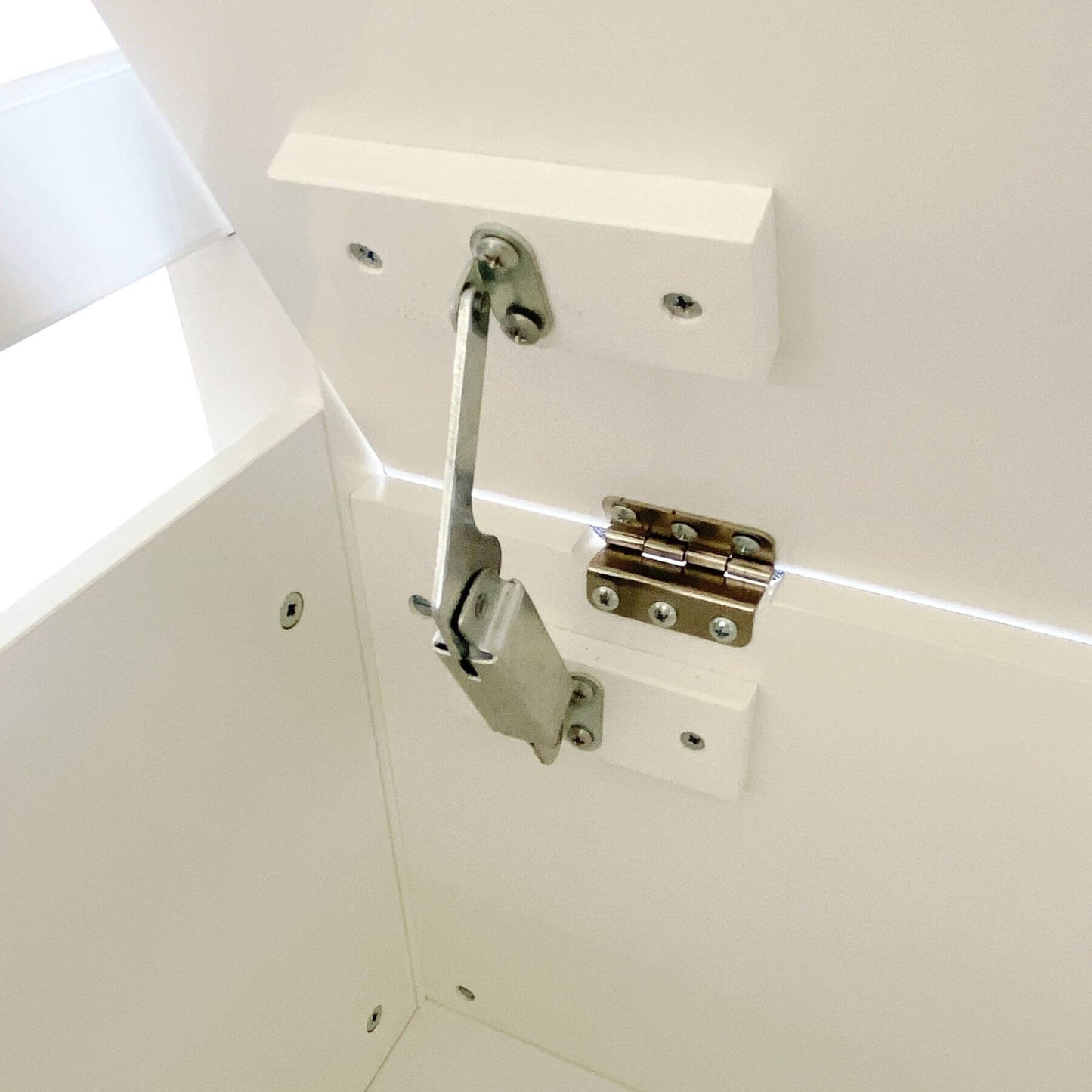 Close-up of a cabinet hinge and latch mechanism on a white surface
