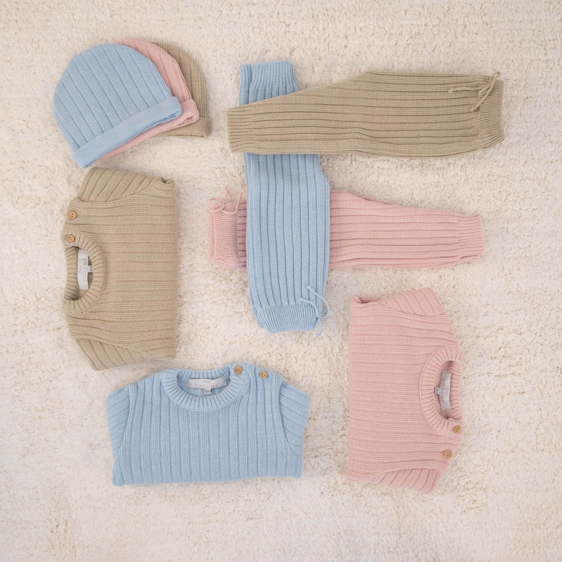 Collection of pastel-colored baby clothes on a soft beige surface