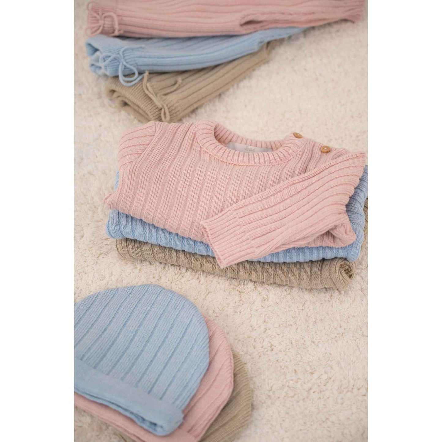 Stack of pastel-colored knit sweaters on a light surface