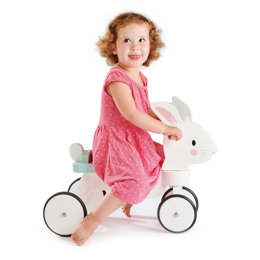 Child in a pink dress riding a white toy horse