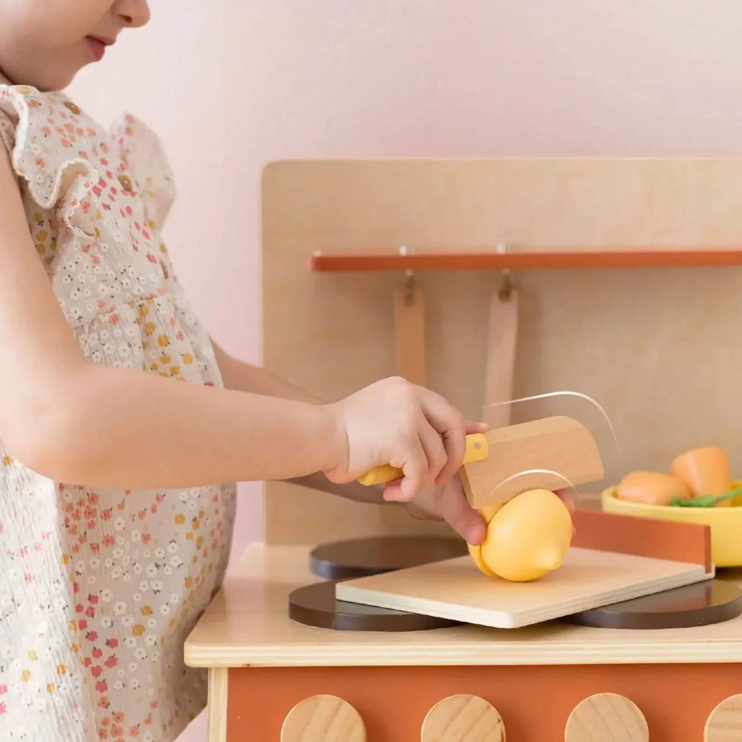 Child playing with Tiny Land® Cubby Kitchenette - Natural, cutting a lemon on a wooden cutting board.