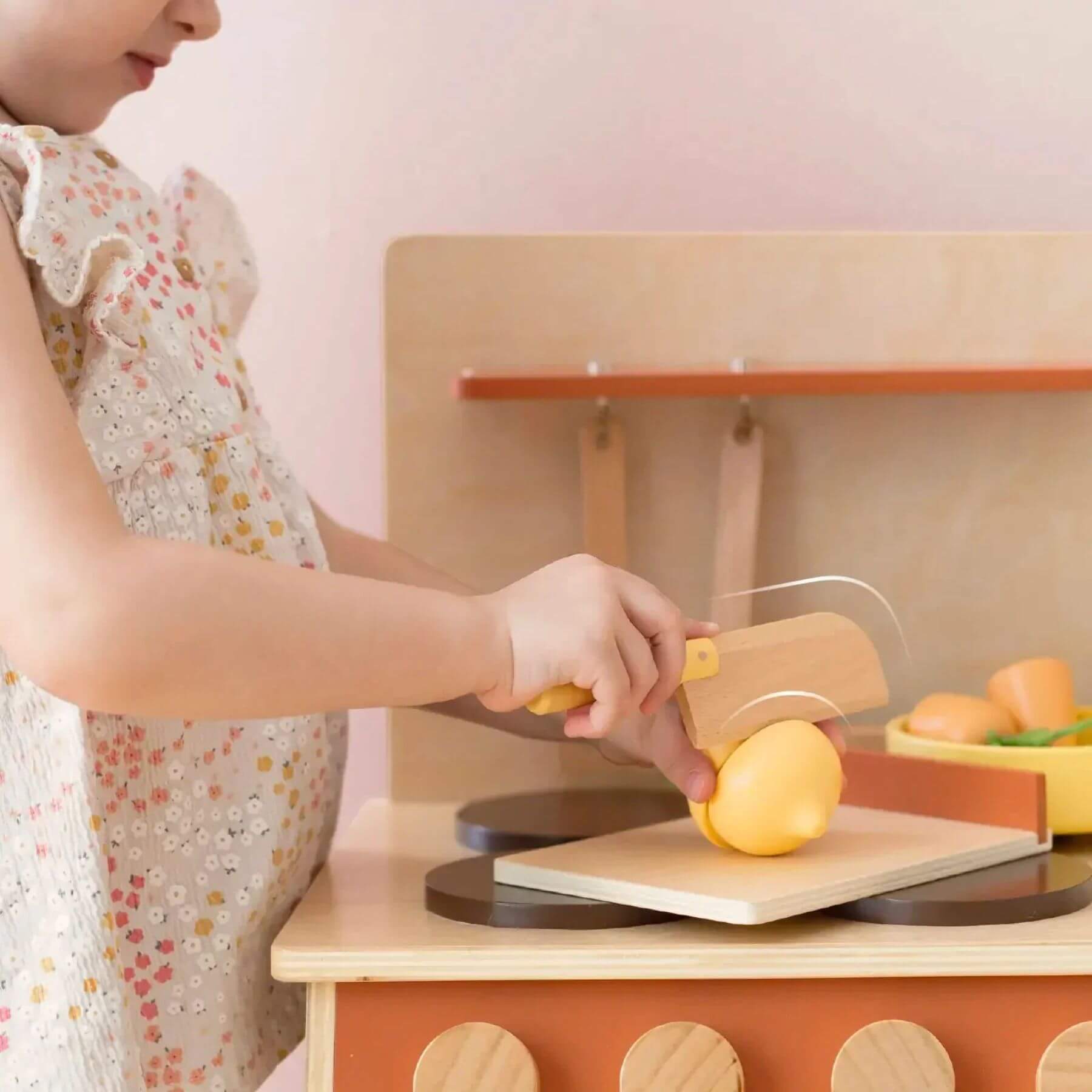 Child playing with Tiny Land® Cubby Kitchenette - Natural, cutting a lemon on a wooden cutting board.