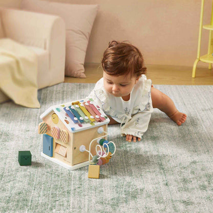 Child playing with a wooden toy house on a carpeted floor.