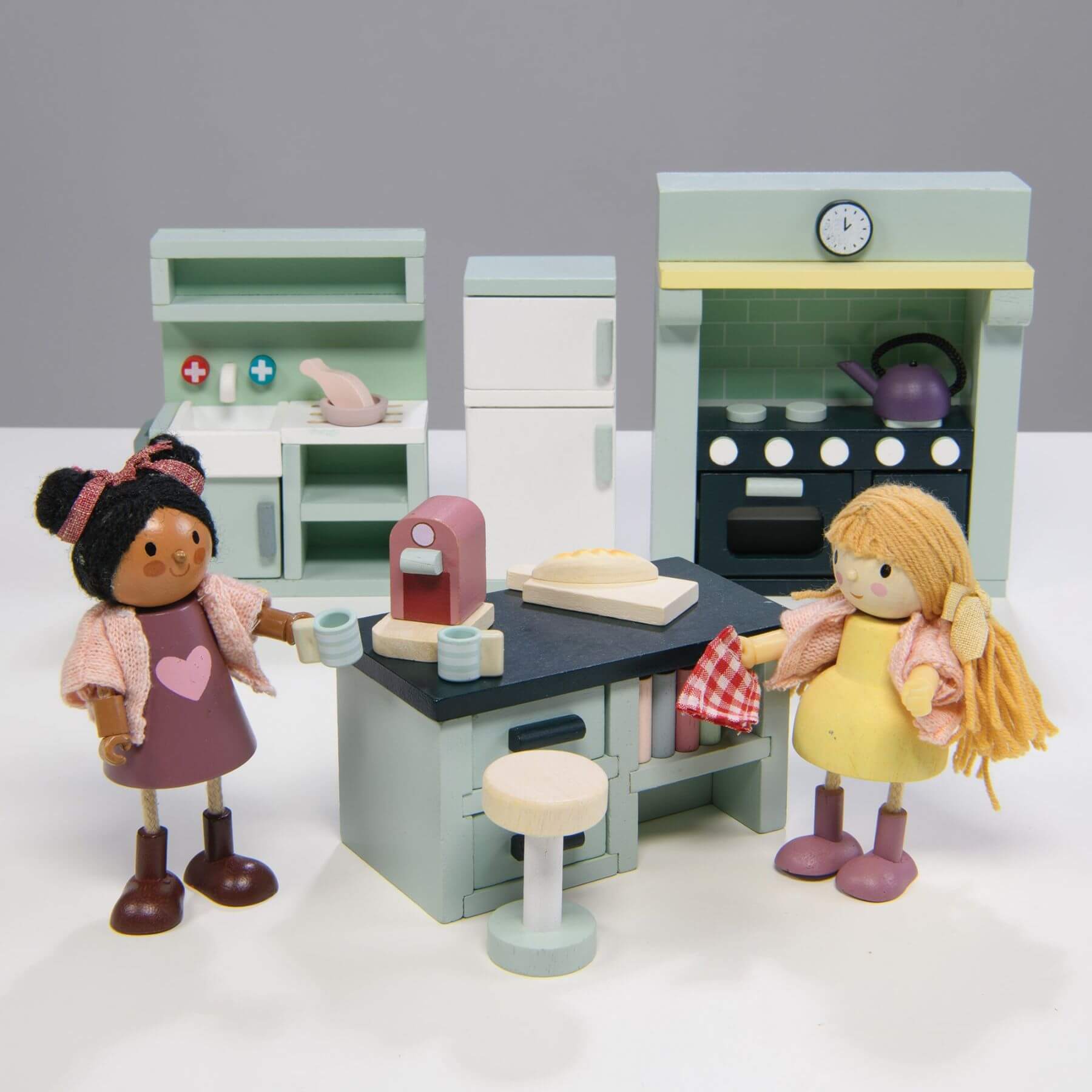 Toy kitchen set with two dolls in front of it on a white background