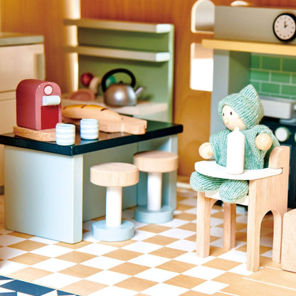 Toy kitchen set with a child's figurine, stools, and kitchen items on a checkered floor.