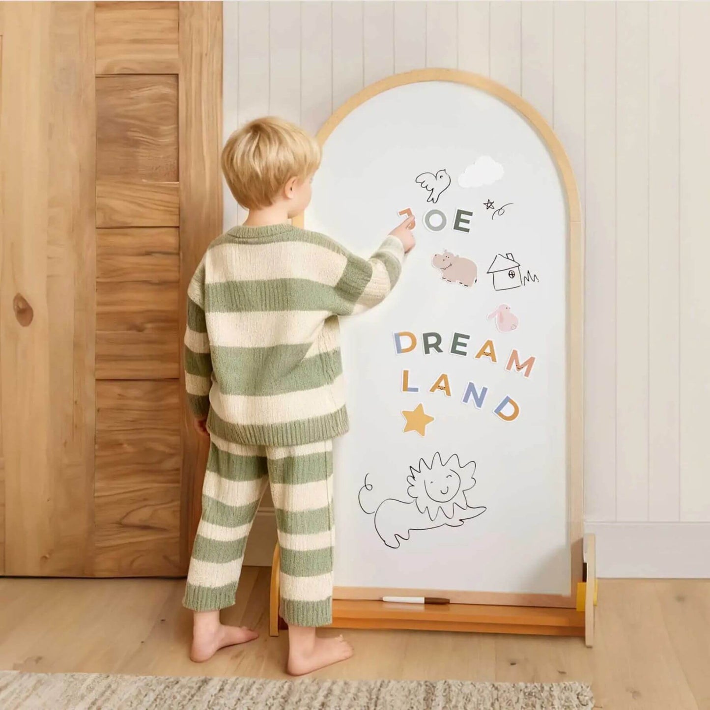 Child in green and white striped pajamas writing on a whiteboard with drawings and the text 'Dream Land'.