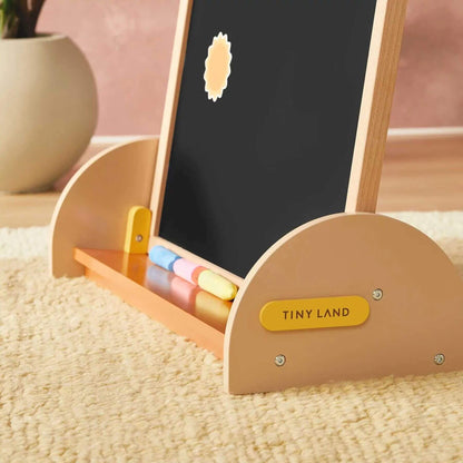 Children's art easel with blackboard and color palette on a carpeted floor, branded 'TINY LAND'.