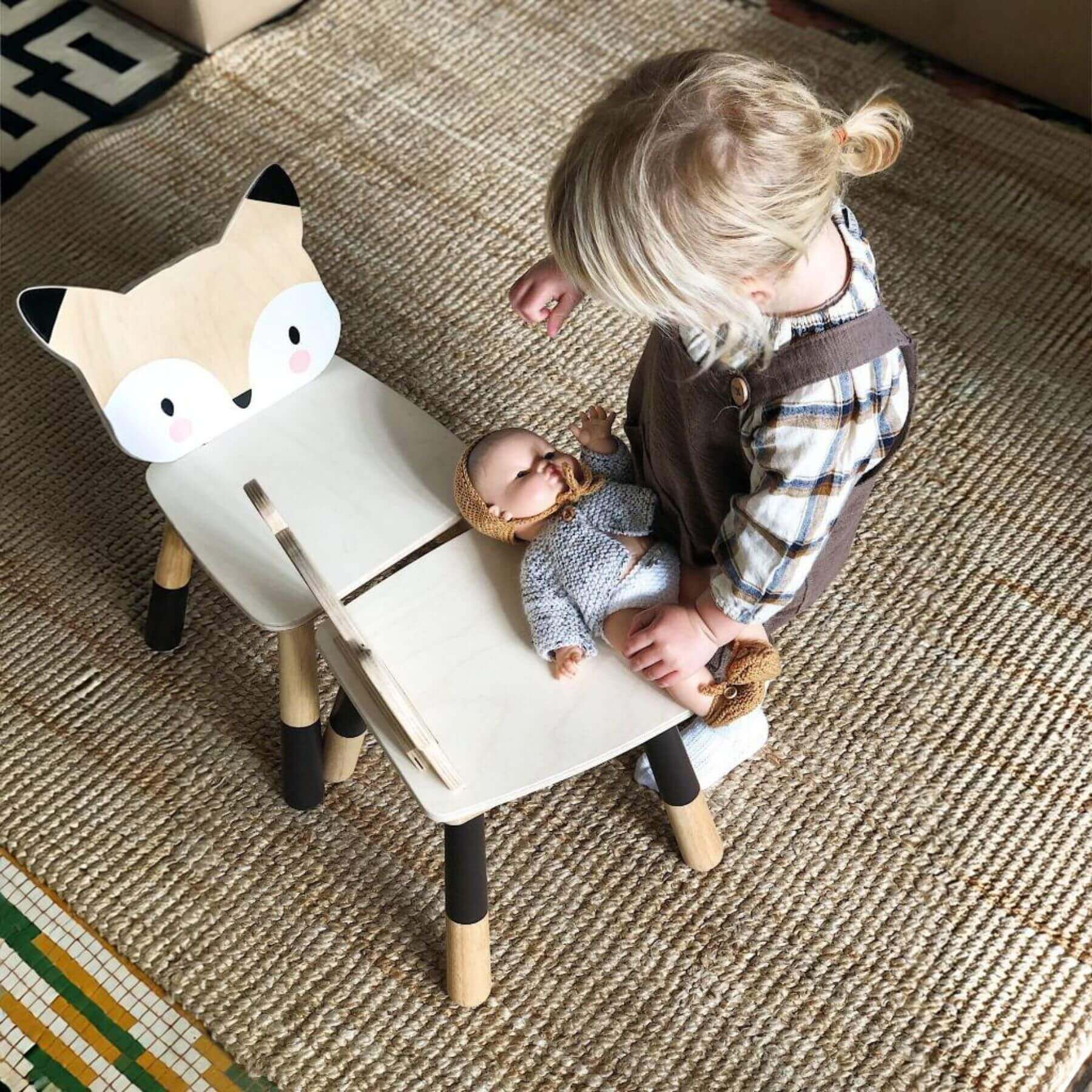 Child playing with a doll on Tender Leaf Forest Fox Chair, on a textured floor.