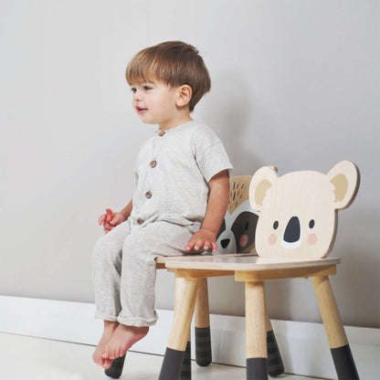 Child sitting on a wooden chair with a koala design against a plain background