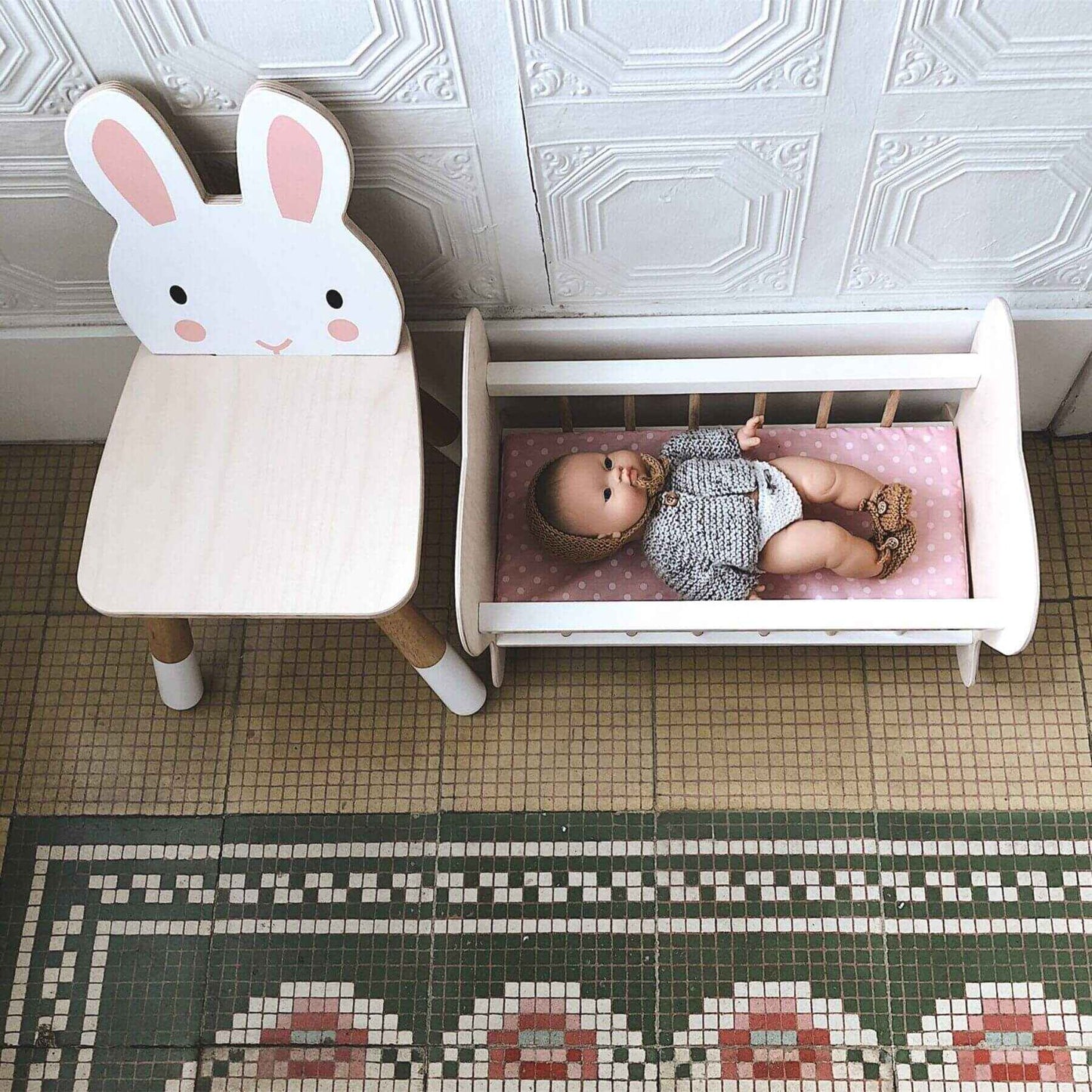 Children's room with Tender Leaf Forest Rabbit Chair and a small bed with a baby doll on a patterned floor.