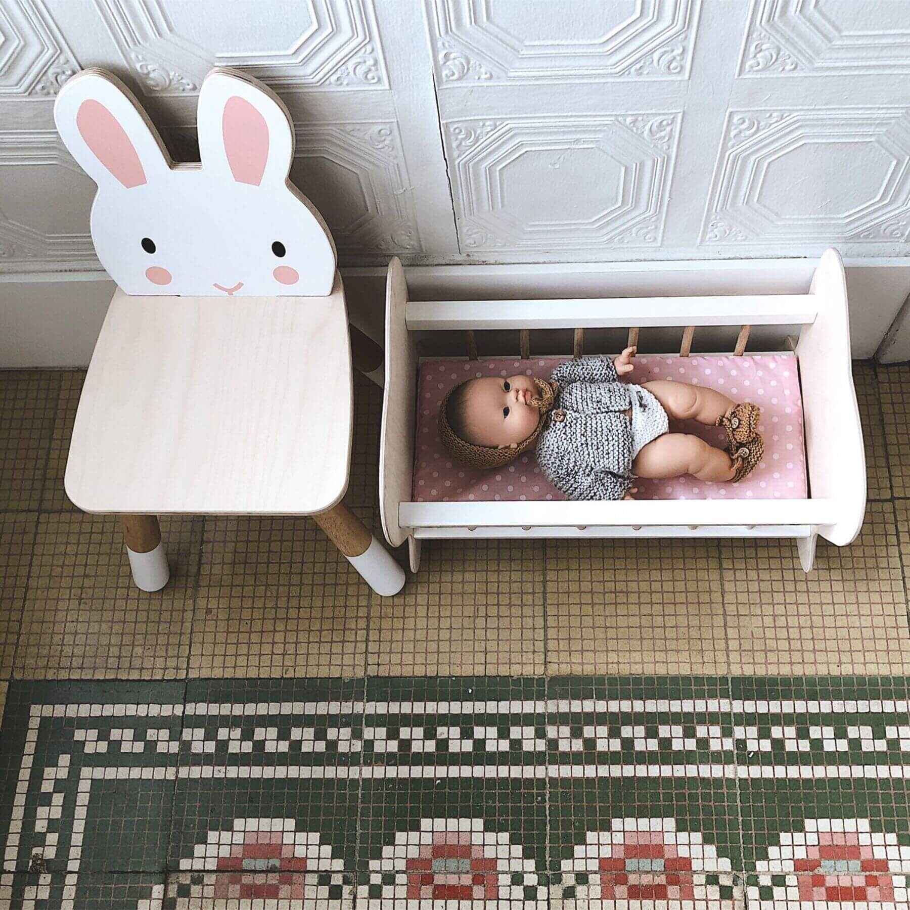 Children's room with Tender Leaf Forest Rabbit Chair and a small bed with a baby doll on a patterned floor.