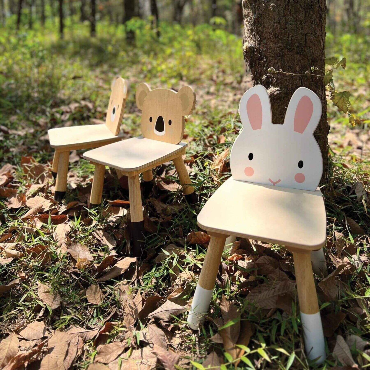 Two children's chairs, two with a bear design and the other with a rabbit design, in a forest setting.