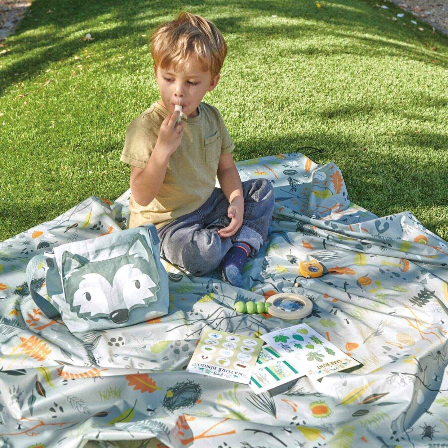 Child sitting on a colorful blanket outdoors with toys and books