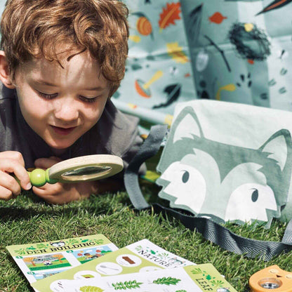 Child playing with a magnifying glass and nature-themed cards on grass