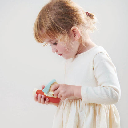 Child in a white dress holding a red and blue toy against a plain background