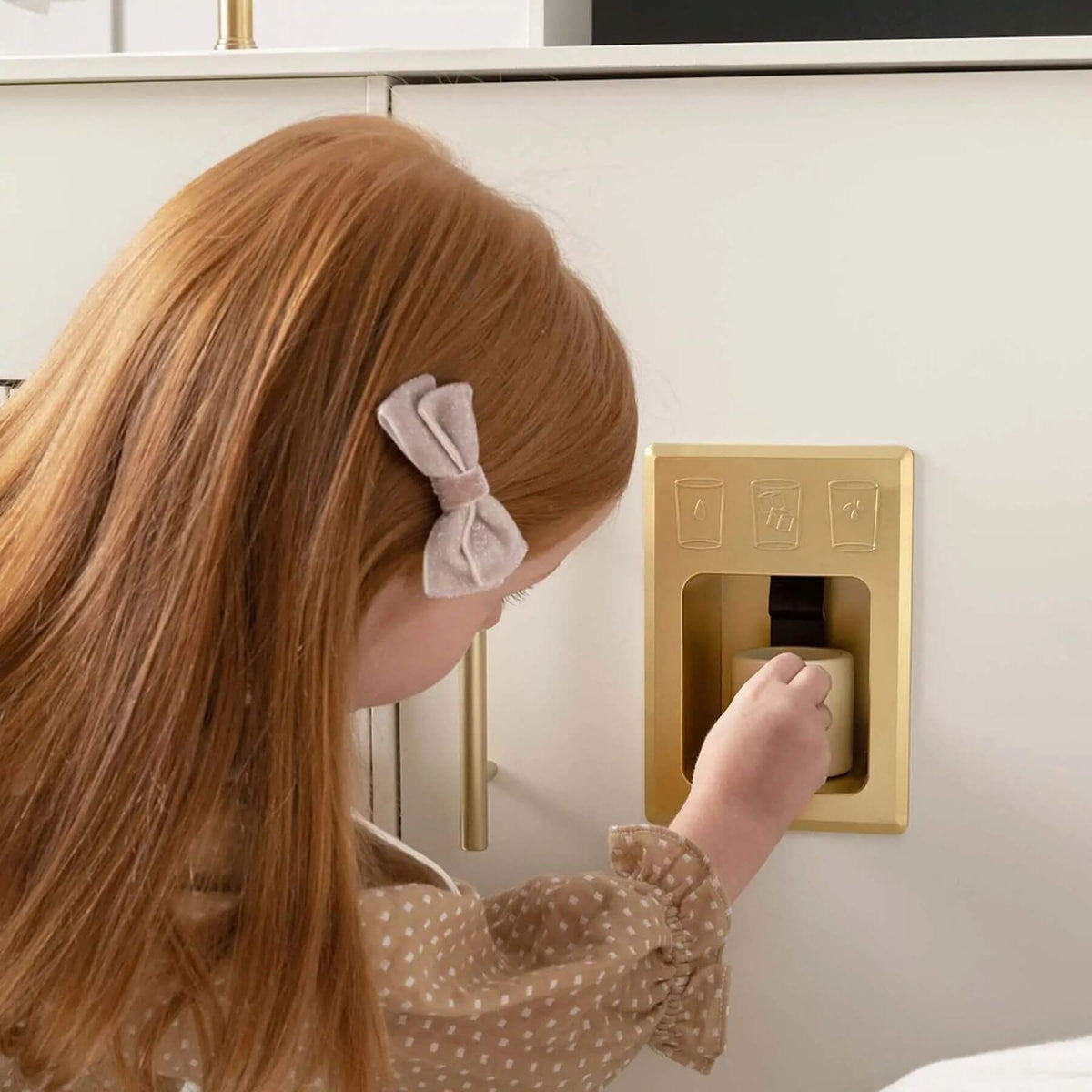 Child using a gold water dispenser on a white cabinet