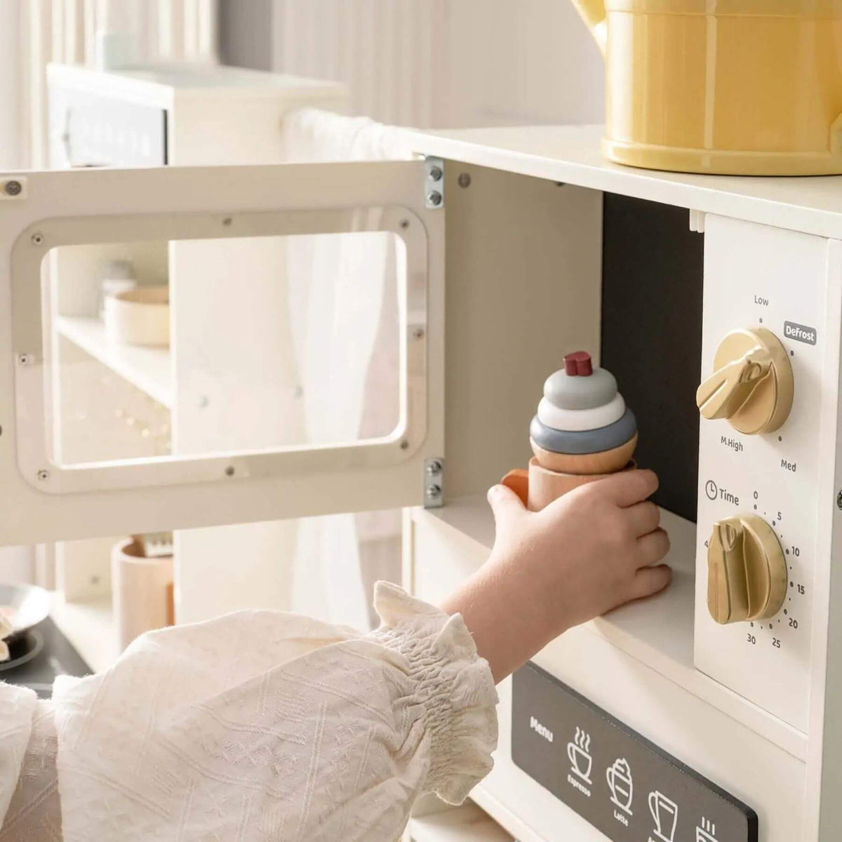 Child's hand placing a stack of wooden toys into a toy microwave oven.