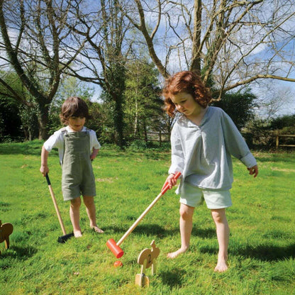 Two children playing with a toy croquet set in a garden.