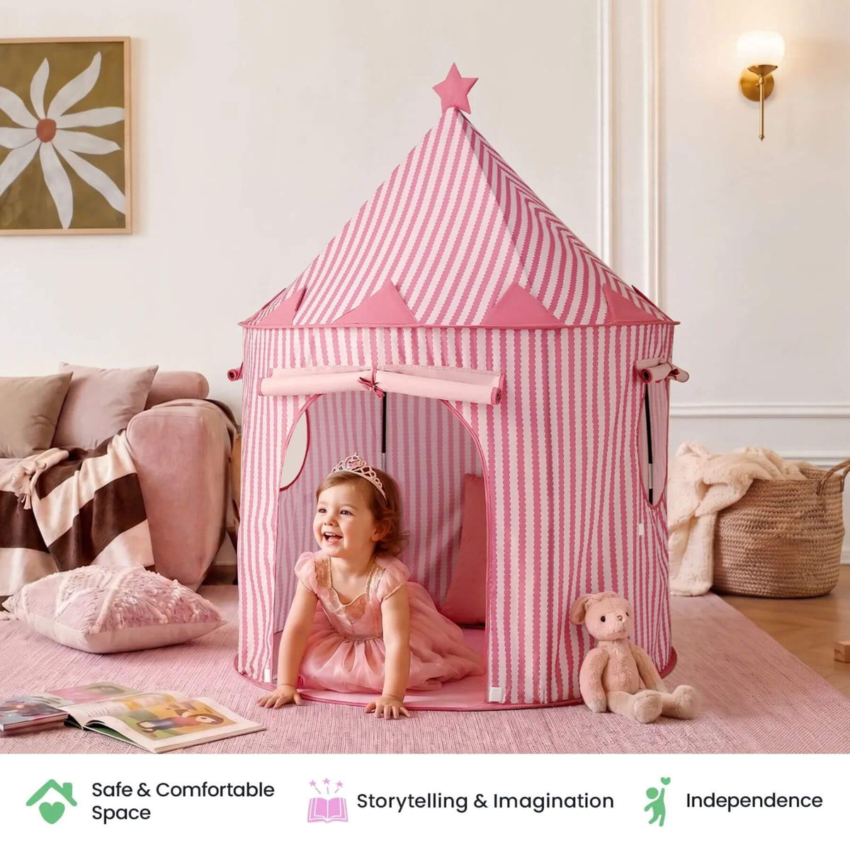 A young child wearing a pink dress crawls inside Tiny Land® Kids Tent - Pink. A teddy bear sits beside the tent, and a sofa and wall decor are visible in the background.