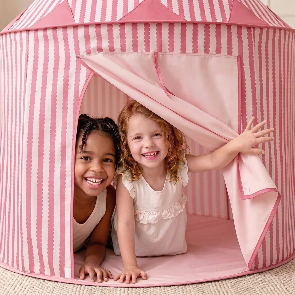 Two young children smiling inside Tiny Land® Kids Tent - Pink, with one child pulling the front flap open.