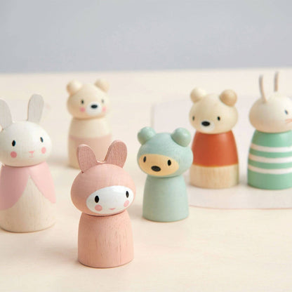 A set of small wooden animal figurines with pastel-colored painted bodies, including bunnies, bears, and a rabbit in a striped outfit, arranged on a light surface against a soft gray background.