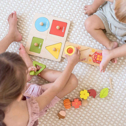Children playing with wooden shape sorting toys on a textured floor.