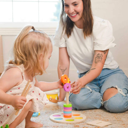 Woman and child playing with colorful wooden toys on a carpeted floor.